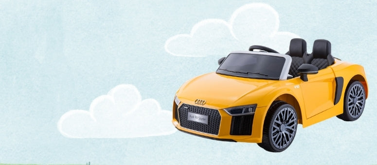 A yellow children's ride-on toy car styled like an Audi R8, shown from a three-quarter front angle against a light blue background with white cartoon clouds.