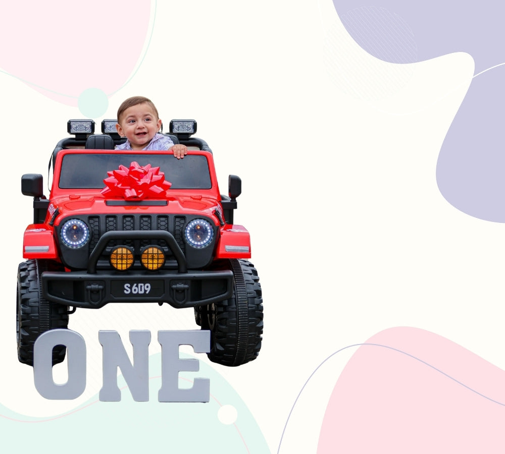 A child sitting in a red ride-on toy jeep with a large red bow on the windshield, set against a pastel abstract background with the word 'ONE' at the bottom.